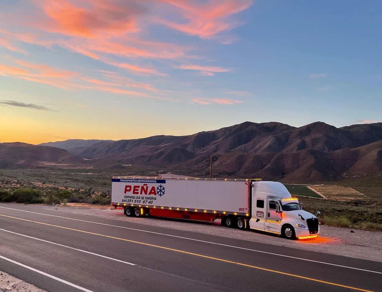 Unidad de Transportes Refrigerados Peña en carretera al atardecer, con las montañas al fondo